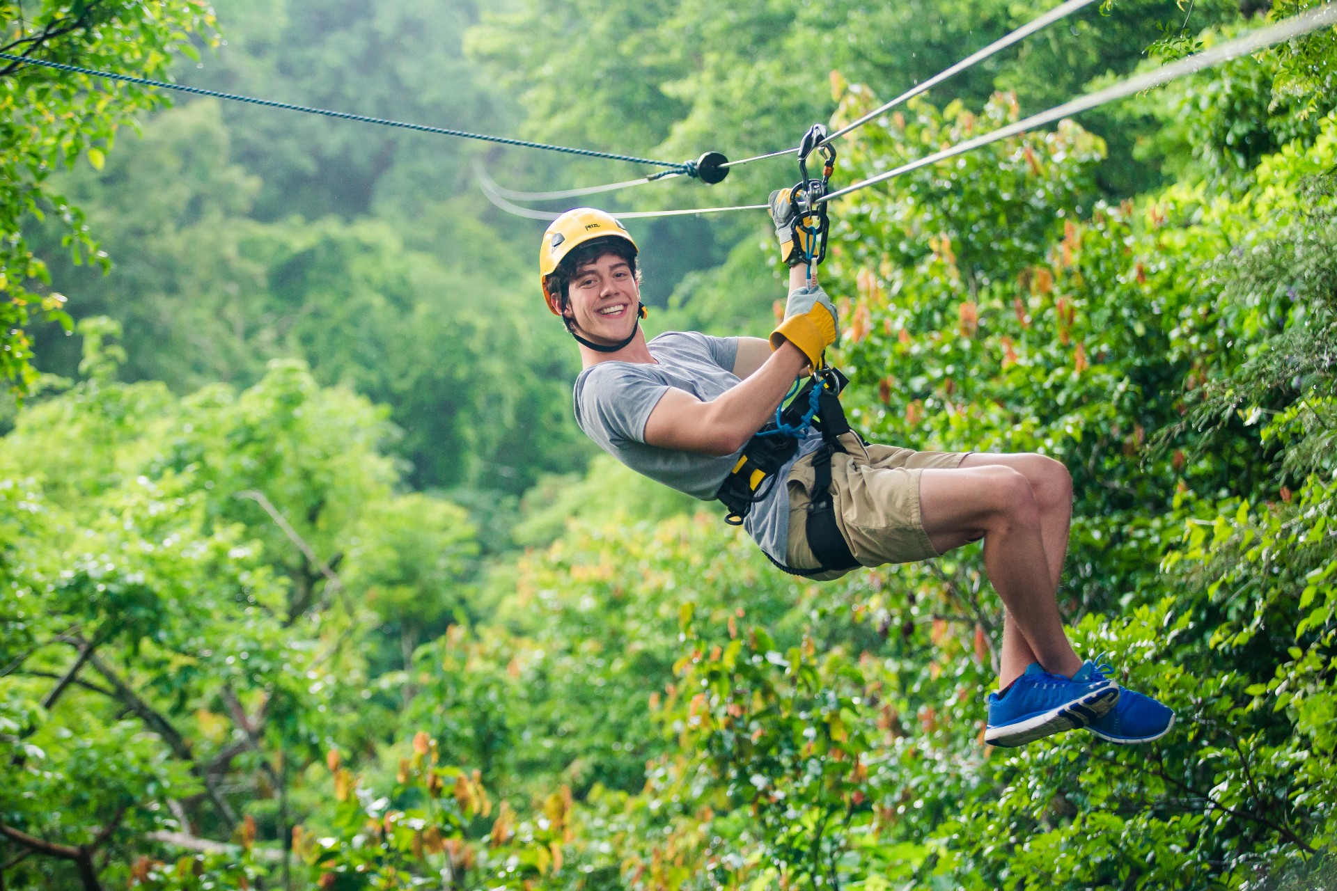 Person zip-lining through lush green forest, smiling and wearing helmet and harness.