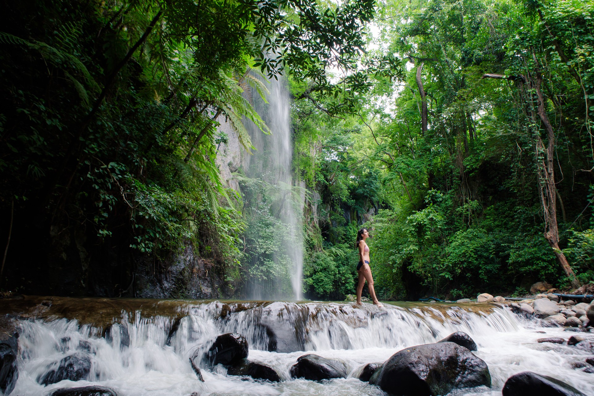 Guest standing near a natural waterfall surrounded by lush green forest