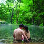 Couple sitting in a serene forest pool surrounded by lush greenery.