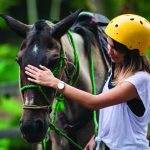 Woman in helmet petting a horse outdoors.