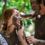 Two people covered in mud laughing and interacting in a green outdoor setting.