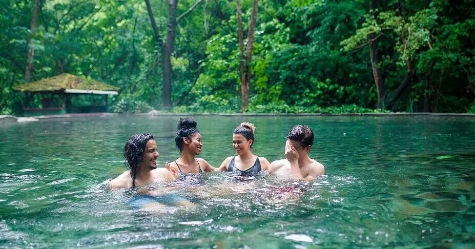 Four people laughing and swimming in a forest pool.