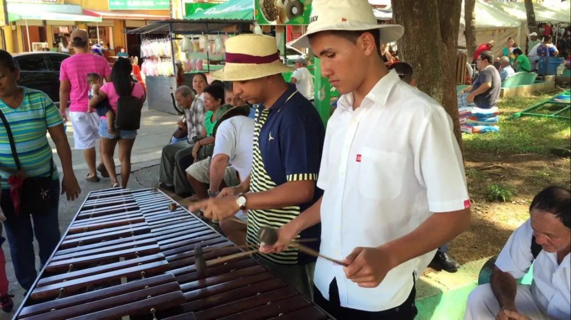 Two men playing a xylophone in an outdoor market setting.