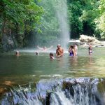 Gente nadando bajo una cascada en un exuberante bosque verde.