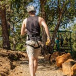 Man in harness walking on forest trail with helmet.