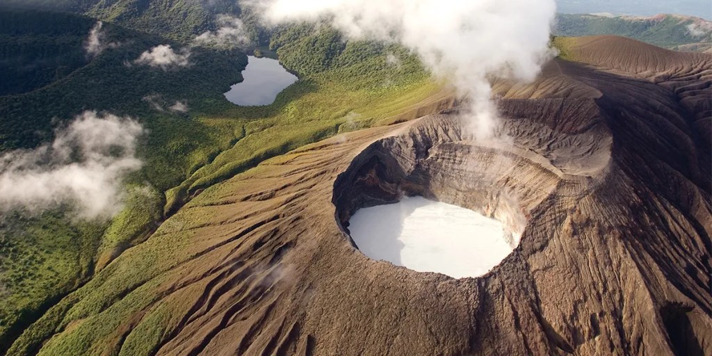 Aerial view of a volcanic crater with surrounding green landscape and a lake.