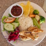 Plate with chicken, rice, beans, salad, plantain, carrots, and broccoli on a speckled countertop.