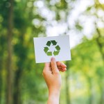 Hand holding a recycling symbol cutout against a blurred forest background.