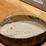 Bowl with light gray clay placed on a wooden surface.