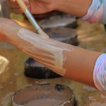 Person applying white paint on their forearm with a brush in a casual setting.