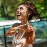 Smiling woman outdoors with lush greenery in the background.