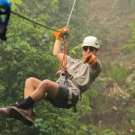 Person ziplining through a lush, green forest wearing safety gear.