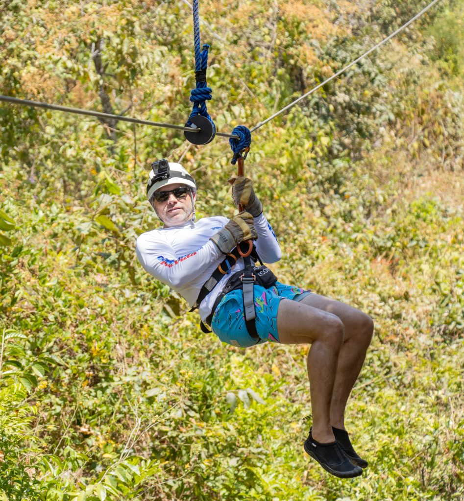 Person zip-lining in outdoor setting wearing helmet and harness.
