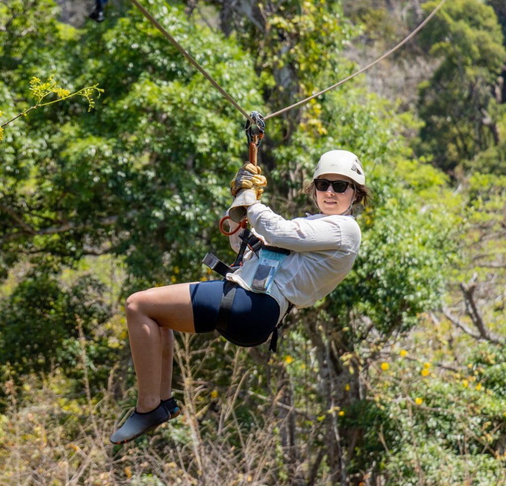 Persona haciendo tirolina por un frondoso bosque verde, con gafas de sol y casco.