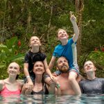 Family of six enjoying time together in a pool surrounded by lush greenery.