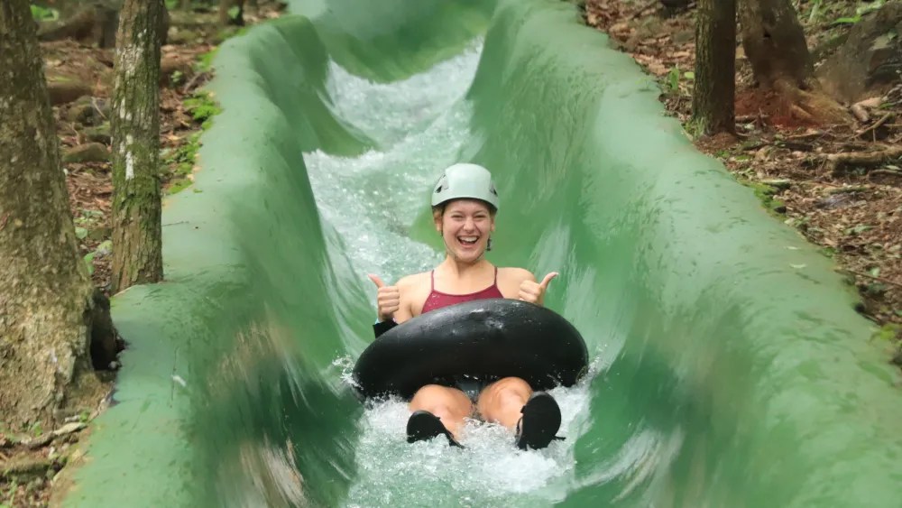 Person smiling on a water slide with a tube, surrounded by trees.