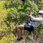Woman zip-lining in outdoor setting with trees in background.