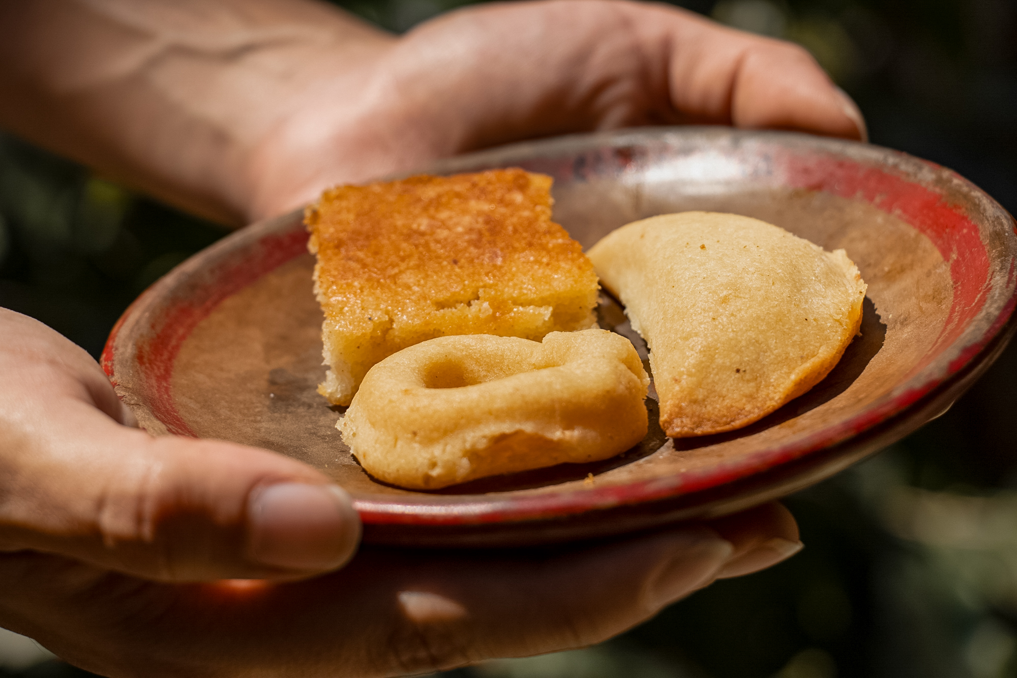 Manos sosteniendo un plato con tres dulces, entre ellos una pequeña tarta y una porción de pastel.