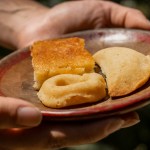 Manos sosteniendo un plato con tres dulces, entre ellos una pequeña tarta y una porción de pastel.
