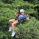 Person zip-lining in a forest, wearing safety gear and smiling.