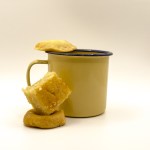 Yellow mug with blue rim and cookies on and beside it on a white background.