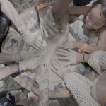 Various hands covered in paint touching a circular canvas on the ground.