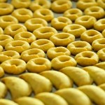 Rows of yellow, ring-shaped and crescent-shaped cookies on a tray.