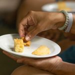 Person holding a plate with pastries, picking one up with their hand.