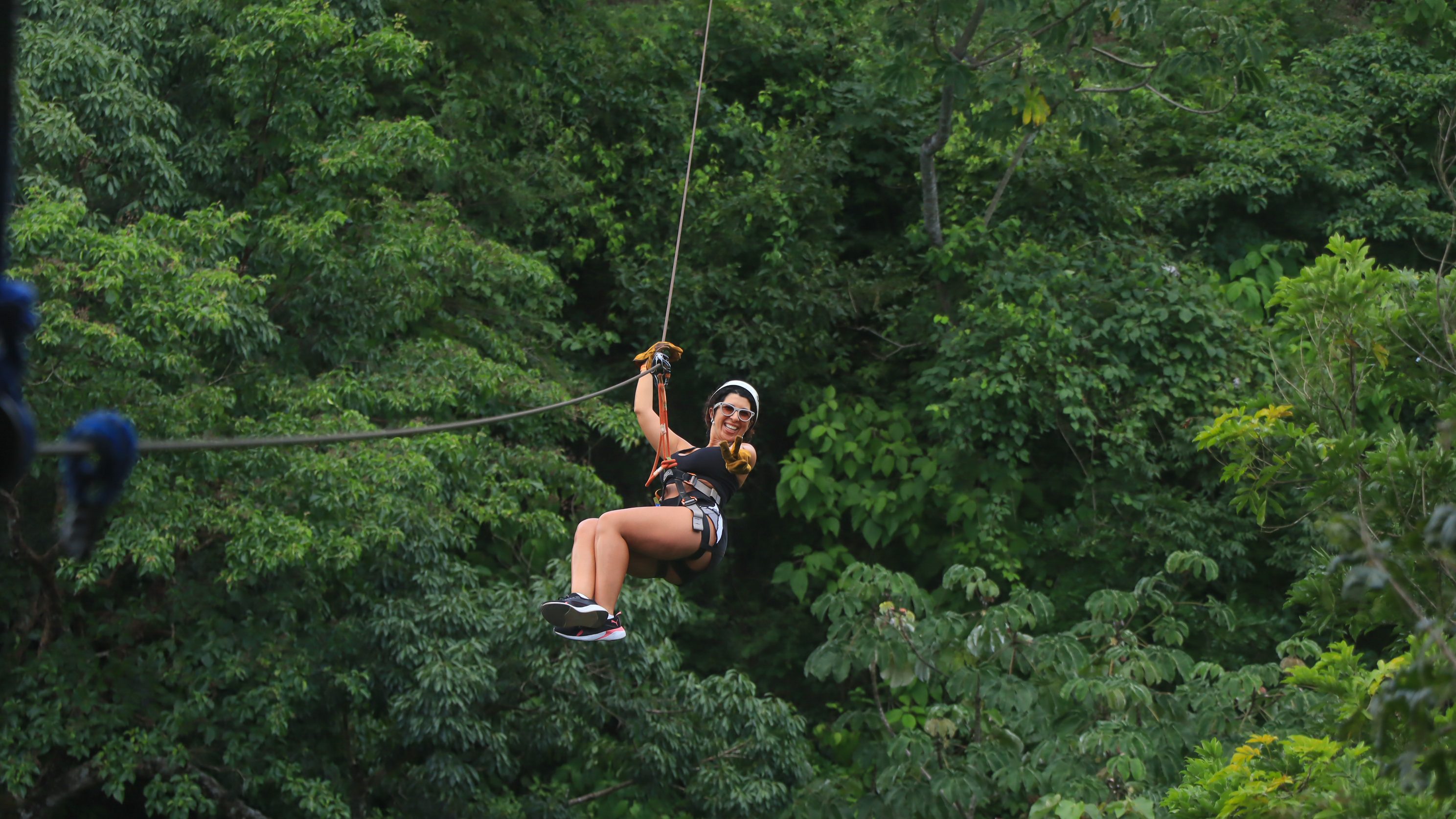 Person ziplining through lush green forest, wearing helmet and safety gear.