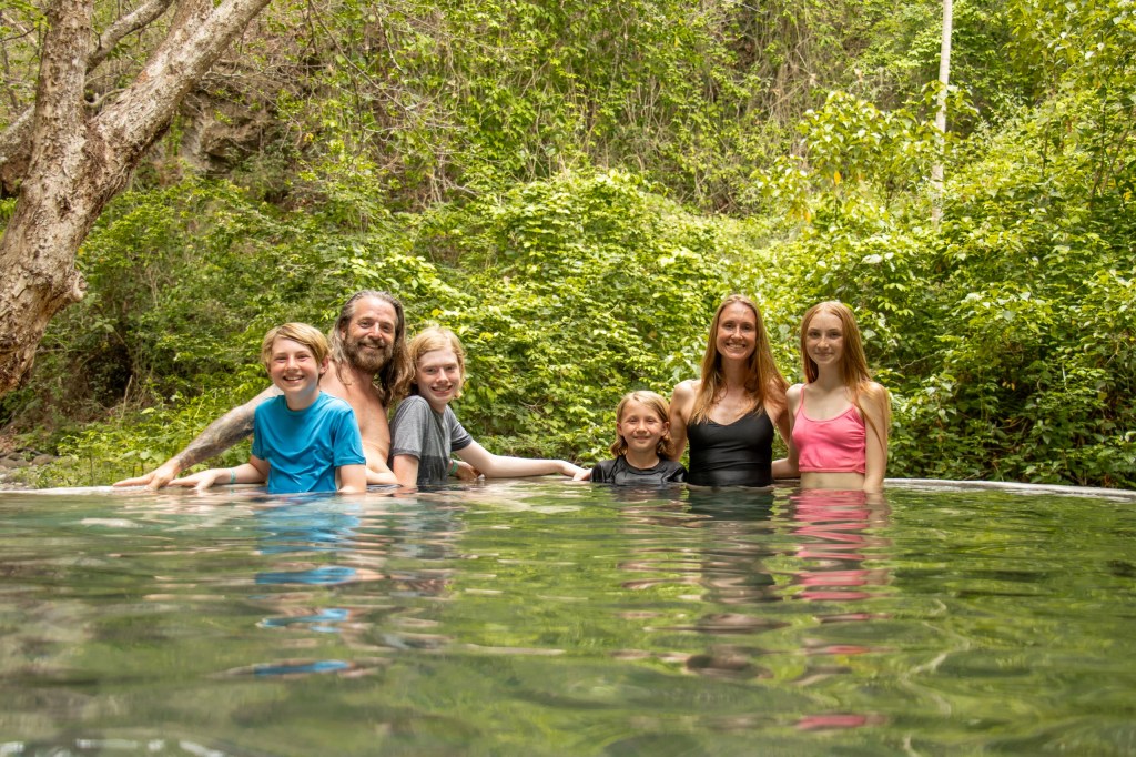 Six people standing in a natural pool surrounded by lush greenery.