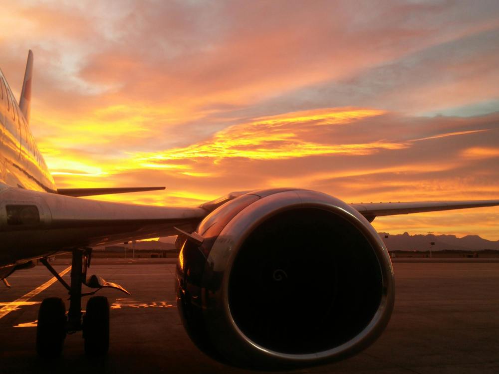 Ala y motor de un avión al atardecer con un cielo vibrante naranja y morado.