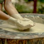 Person's arms dipping into a large bowl of liquid clay outdoors.