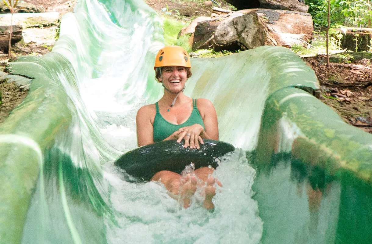 Person in helmet tubing down a water slide surrounded by greenery.