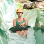 Person in helmet tubing down a water slide surrounded by greenery.
