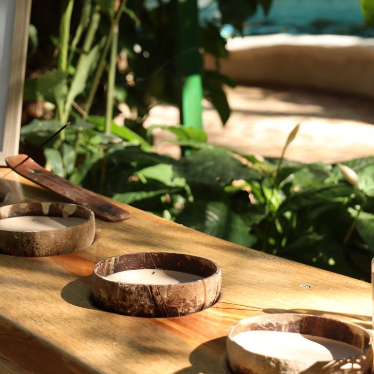 Wooden candle holders with unlit candles on a table in a garden setting.