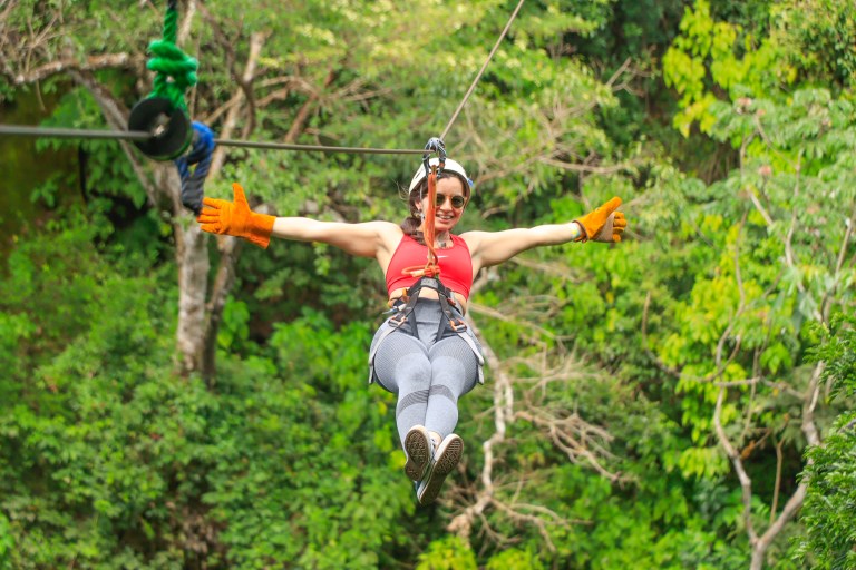 Person ziplining through forest with arms outstretched, wearing gloves and a harness.