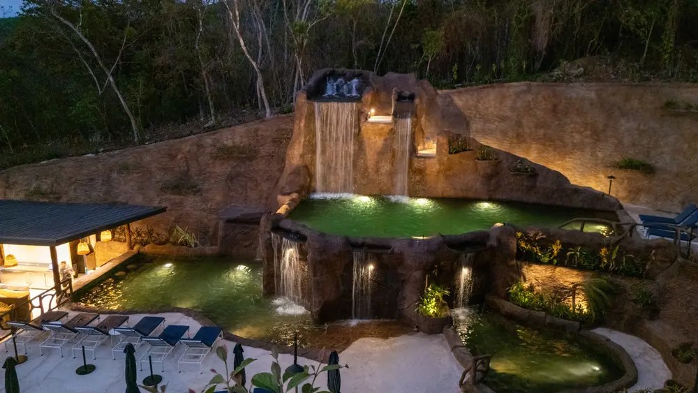 Natural-themed volcanic pools at Rincon Thermals with waterfalls, lounge chairs, and surrounding trees at dusk