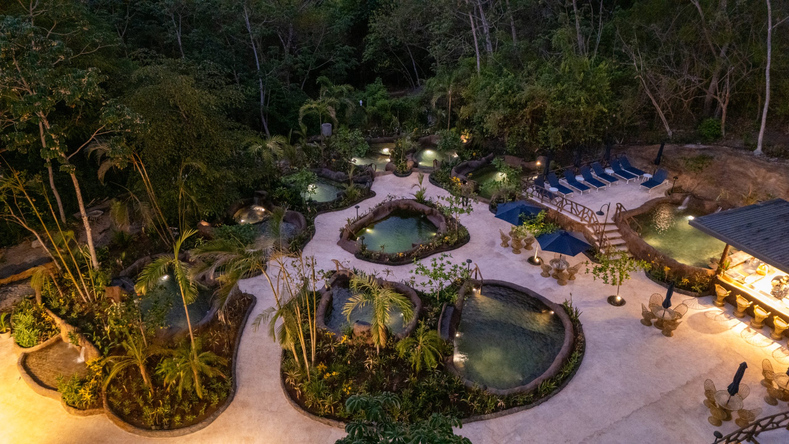 Aerial view of illuminated outdoor pools surrounded by lush greenery.