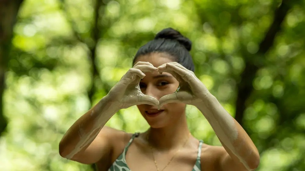Persona forma corazón con las manos, fondo verde.