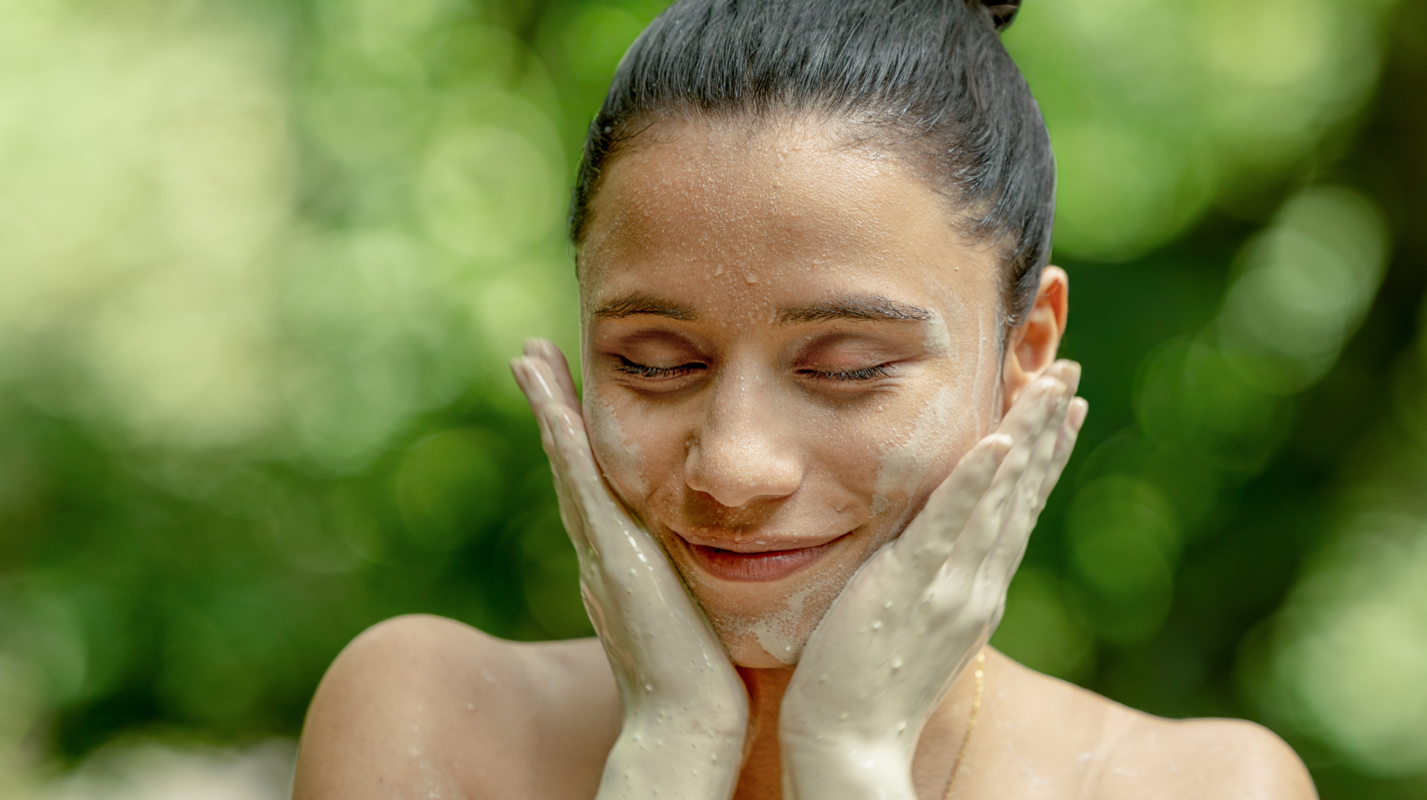 Woman smiling with closed eyes and hands on face, green background.