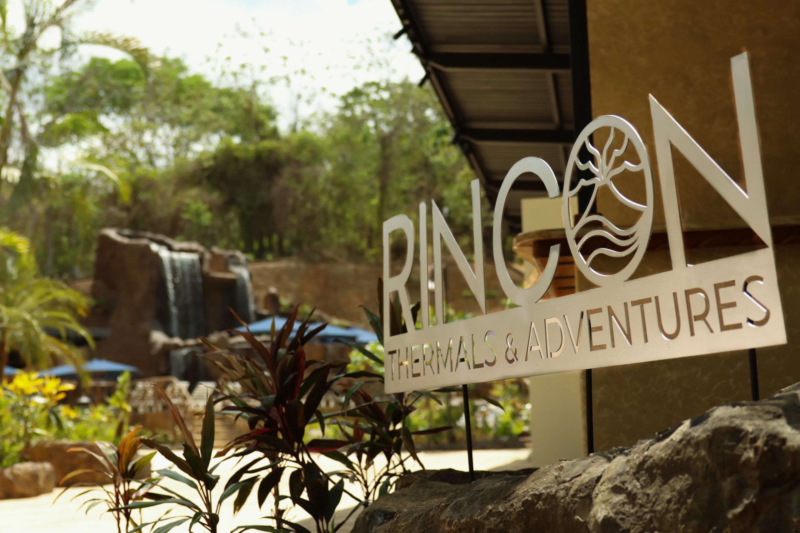 Rincon Thermals and Adventures welcome sign near a waterfall and tropical foliage at the entrance