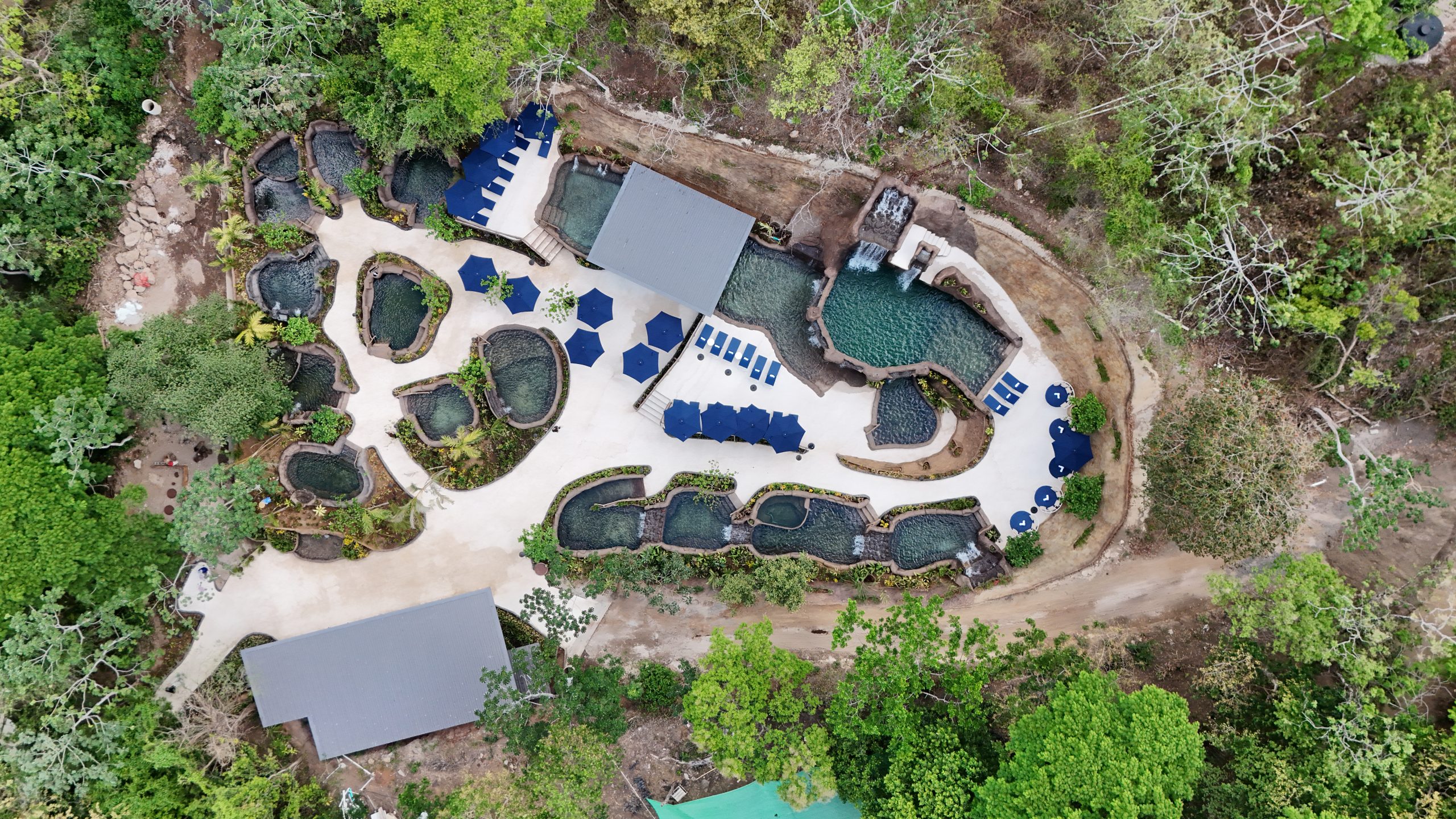 DJI_20260425112032_0160_D Aerial view of pools in a lush forest setting with surrounding pathways.