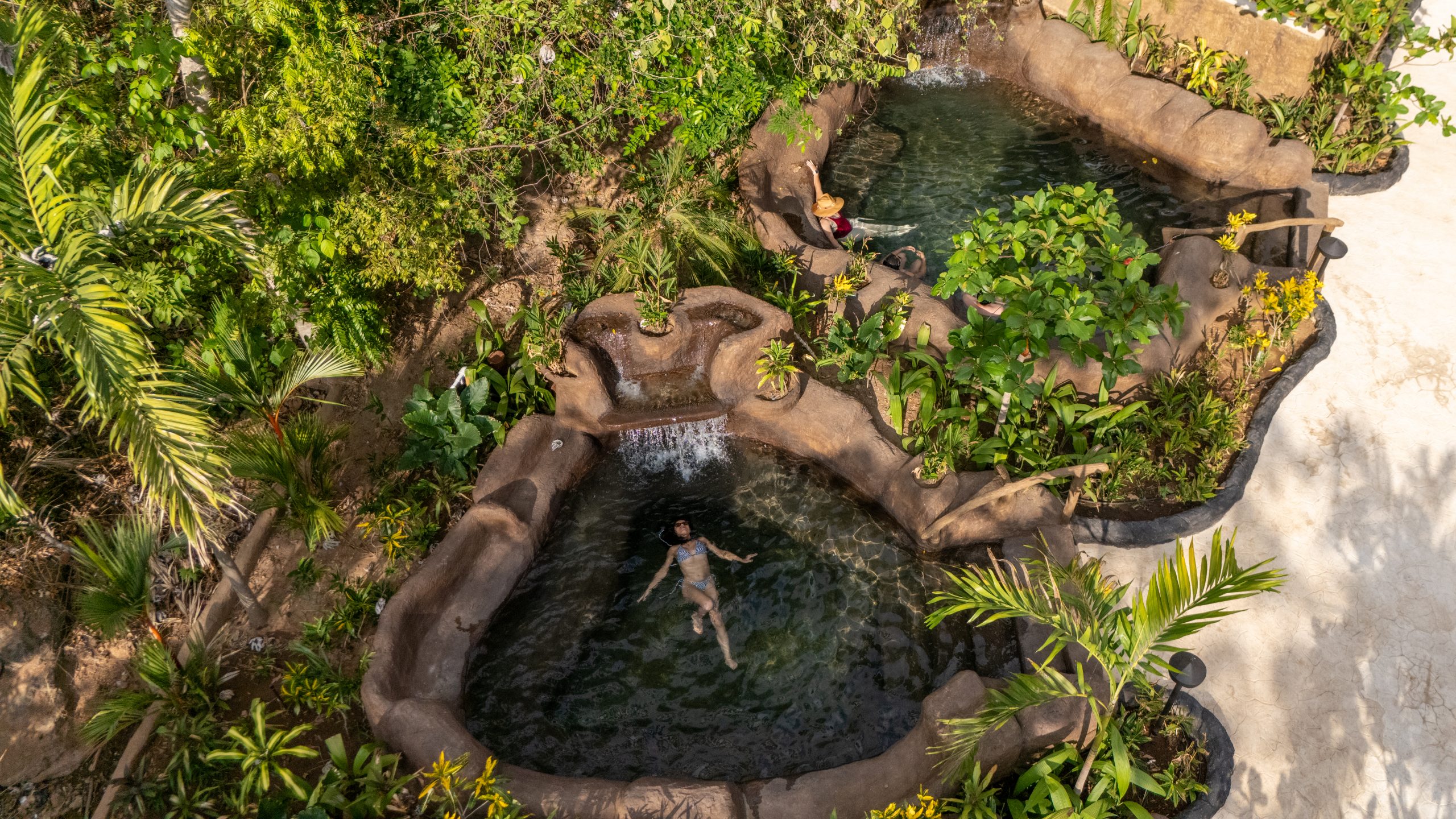 Two people relaxing in naturalistic stone hot tubs surrounded by greenery.