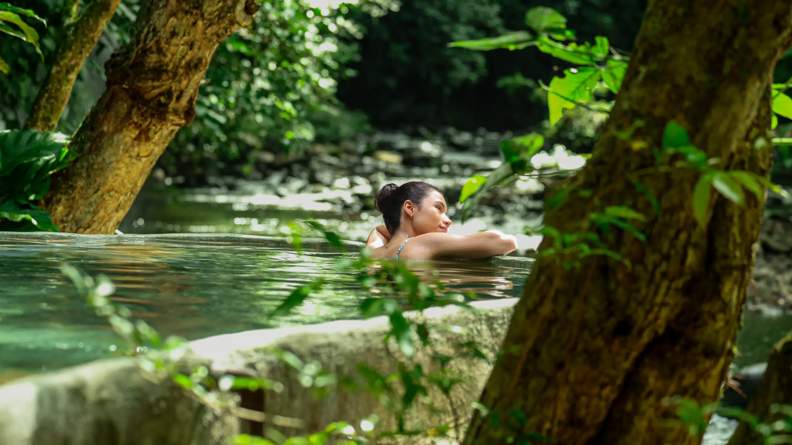 Person relaxing in a natural volcanic pool surrounded by trees and greenery at Rincon de la Vieja