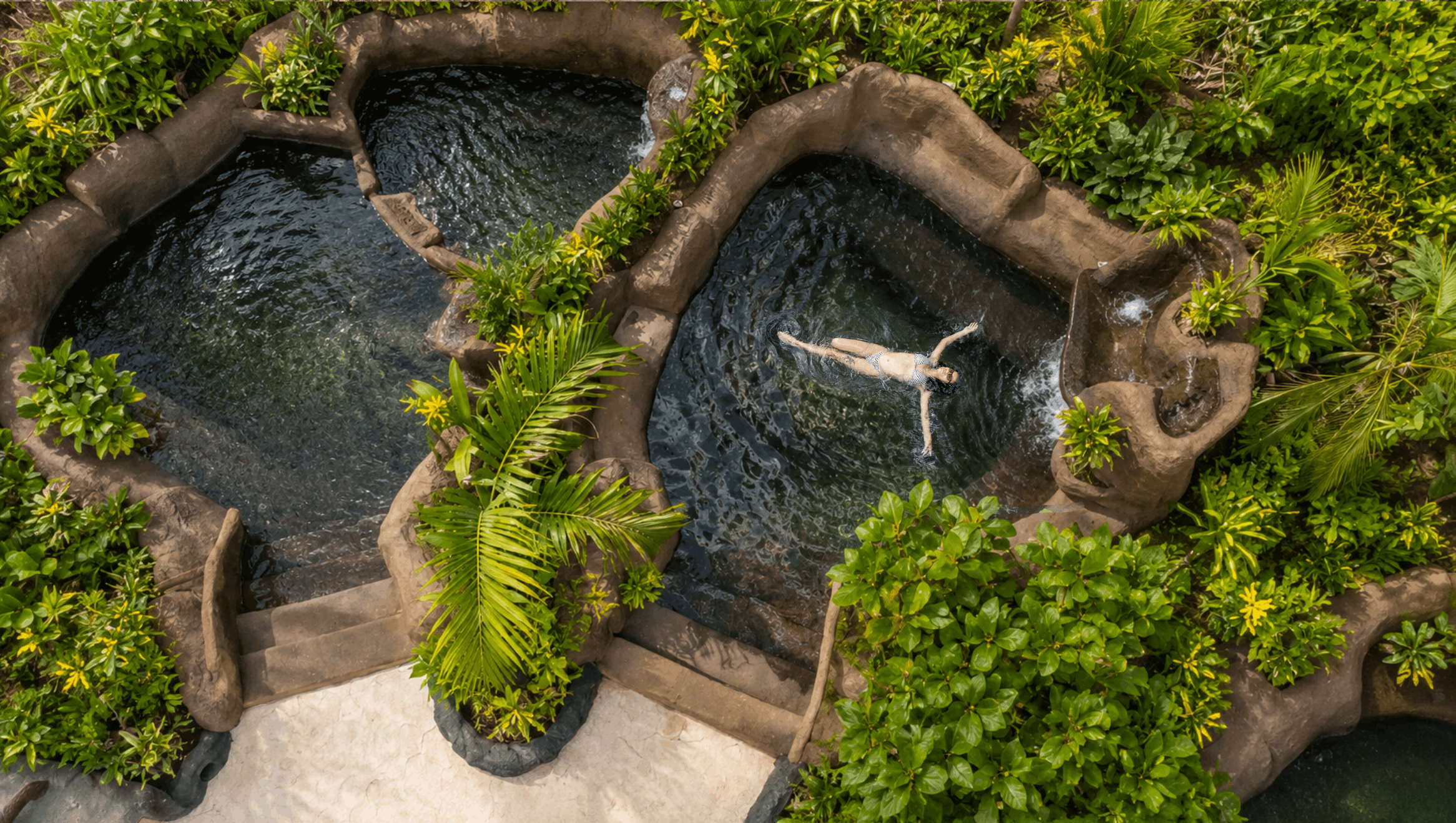 Person floating in a natural hot spring pool surrounded by lush greenery.