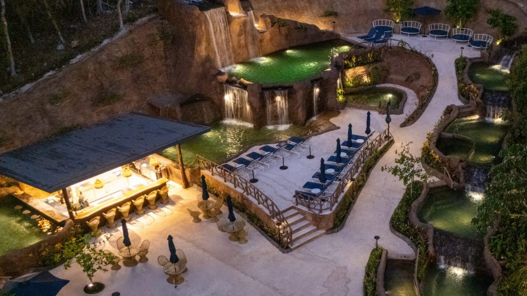 Aerial view of an illuminated outdoor spa with pools and seating areas at night.