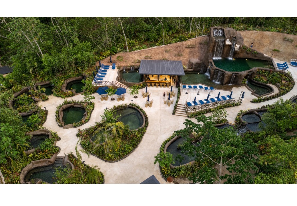 Aerial view of a tropical resort with pools, lounge chairs, and waterfalls.