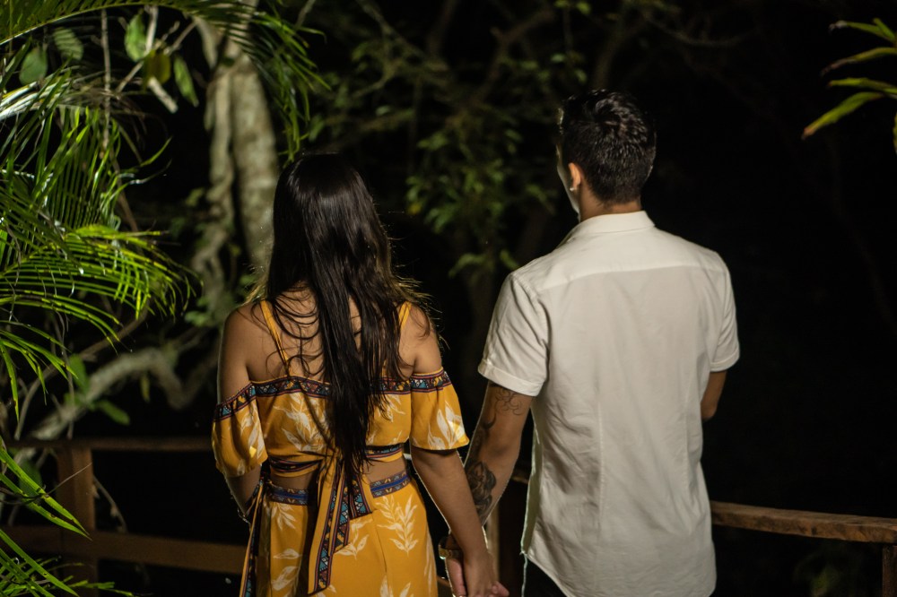 Couple holding hands, walking at night surrounded by trees.