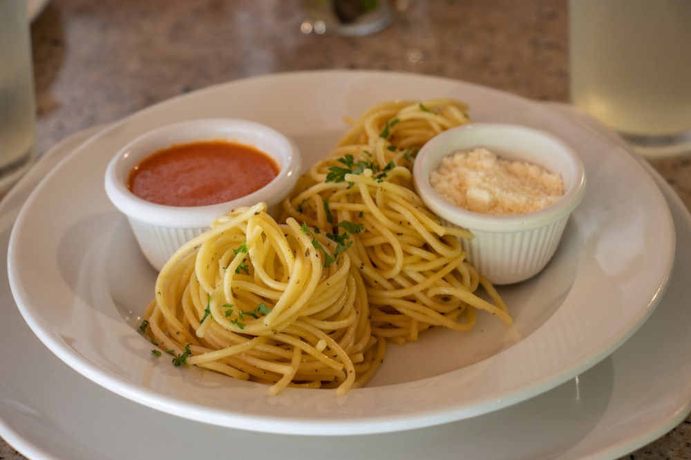 Plate of spaghetti with parsley, tomato sauce, and Parmesan cheese in small bowls on the side.