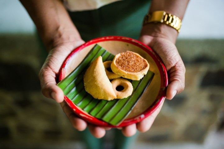 Person holding a plate with assorted pastries on a banana leaf.
